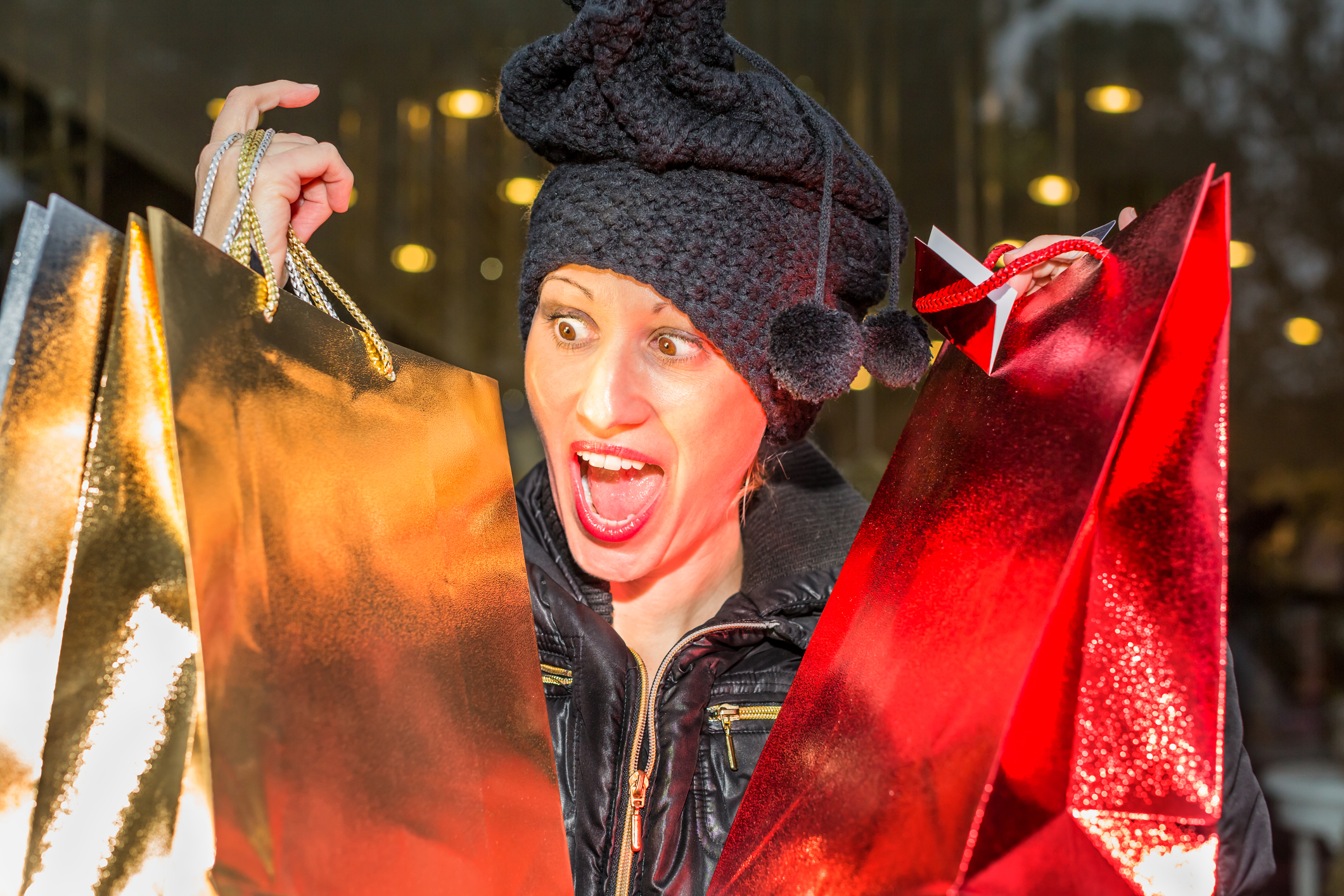 Woman with winter hat on holding up gold and red shopping bags for December holidays..