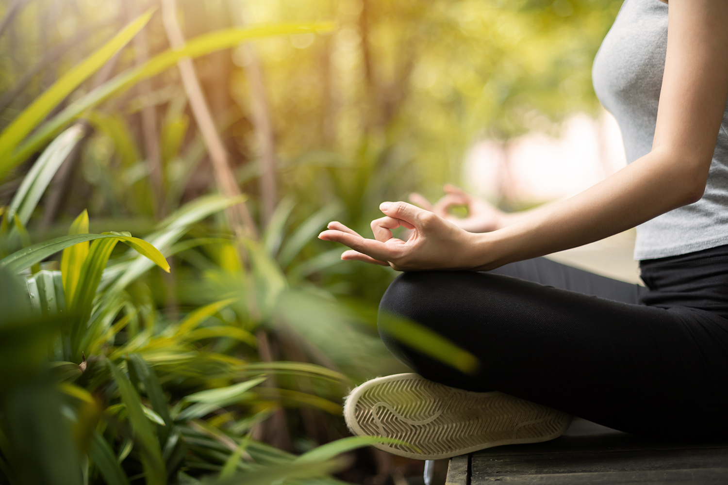 a woman meditating outside, surrounded by plants