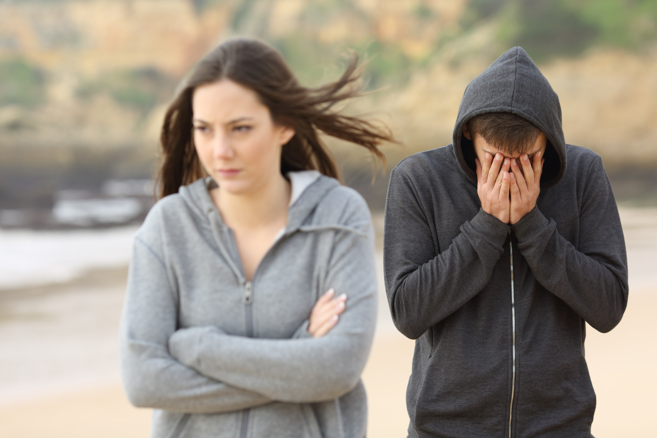 Young woman with arms crossed turned away from young man with face in his hands.