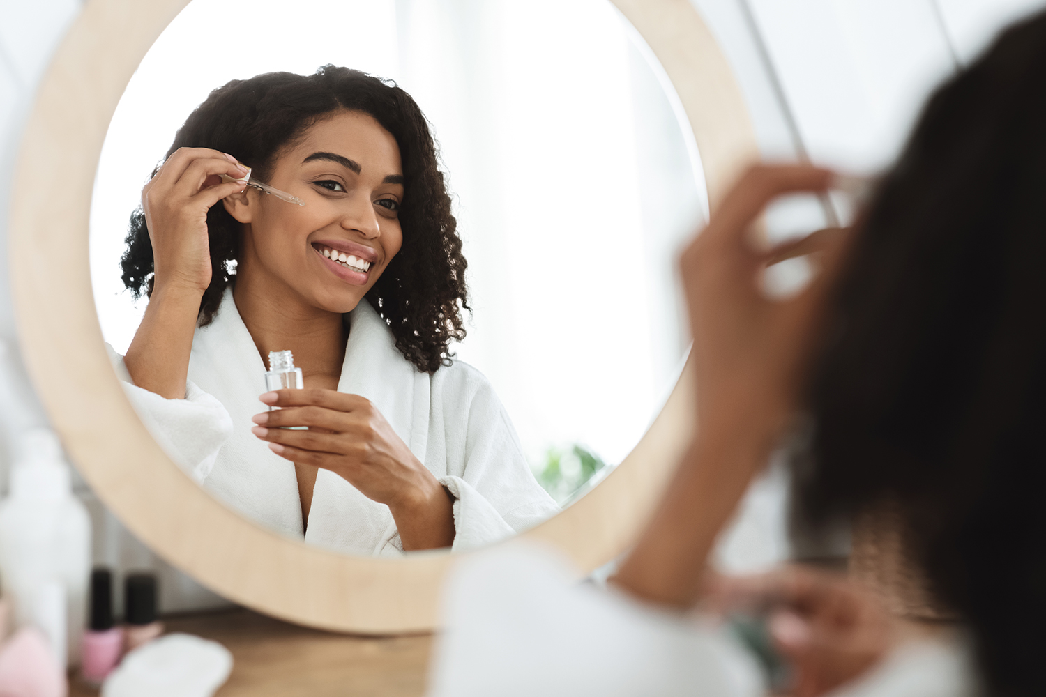 a woman applying serum to her face in the mirror