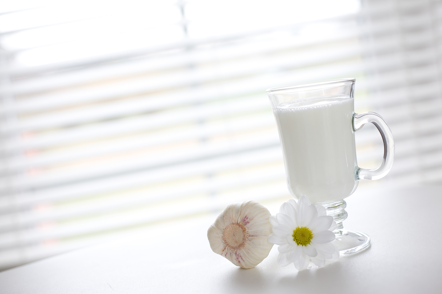 A glass of milk next to a clove of garlic and a fresh flower