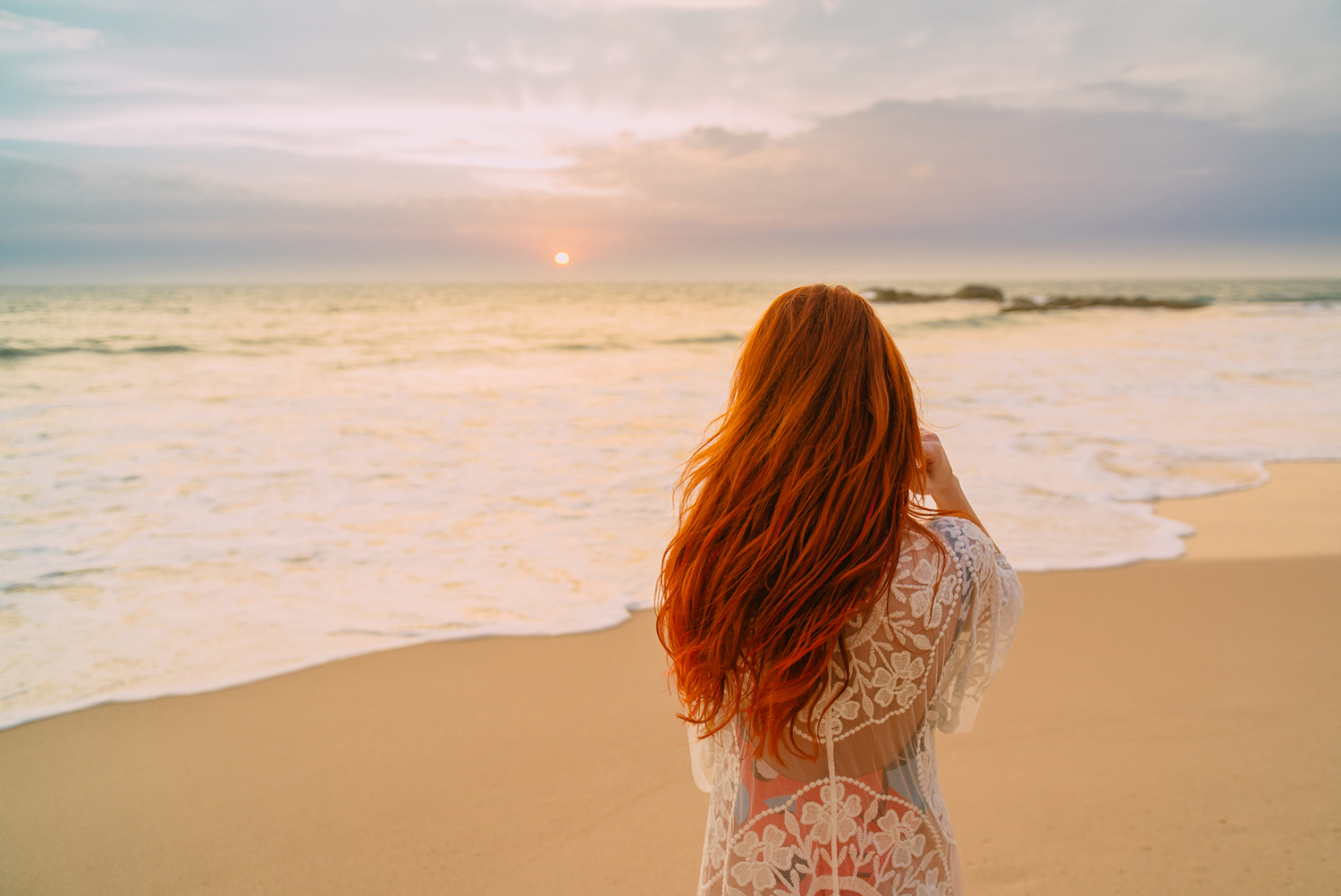 Red head woman on the beach looking at the sea.