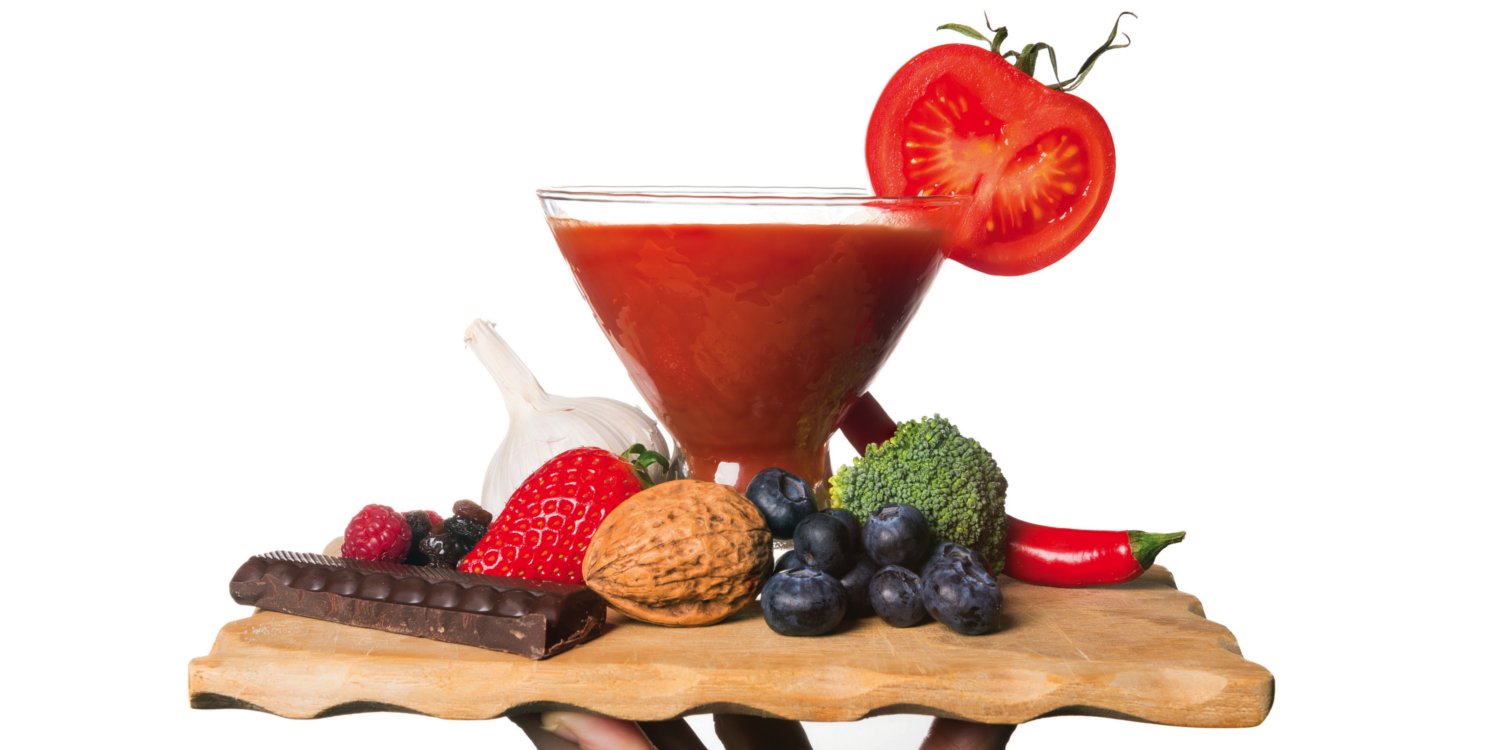 Hand holding dish of cancer fighting foods, including smoothie, tomatoes, broccoli and blueberries