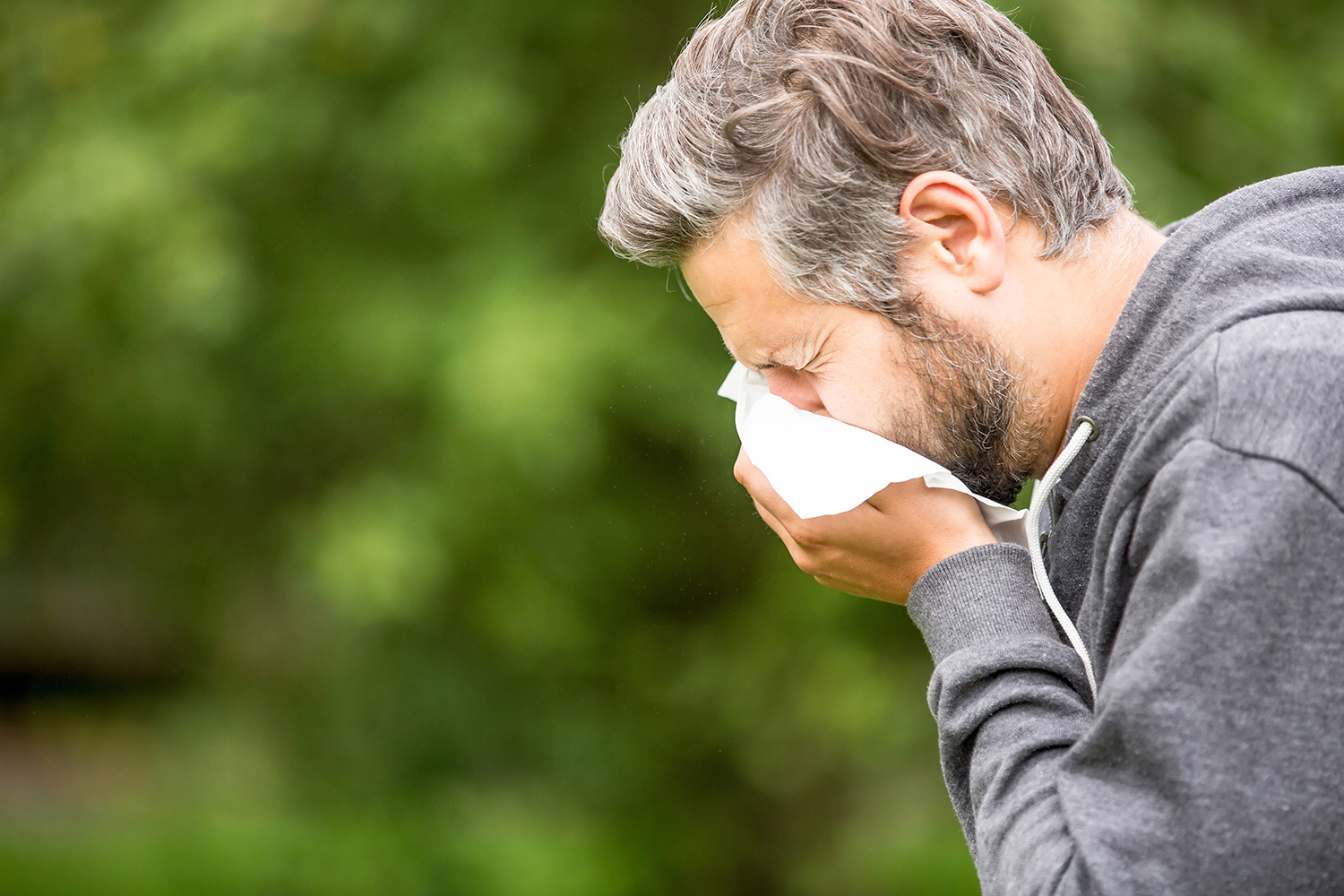a middle-aged man sneezing into a tissue