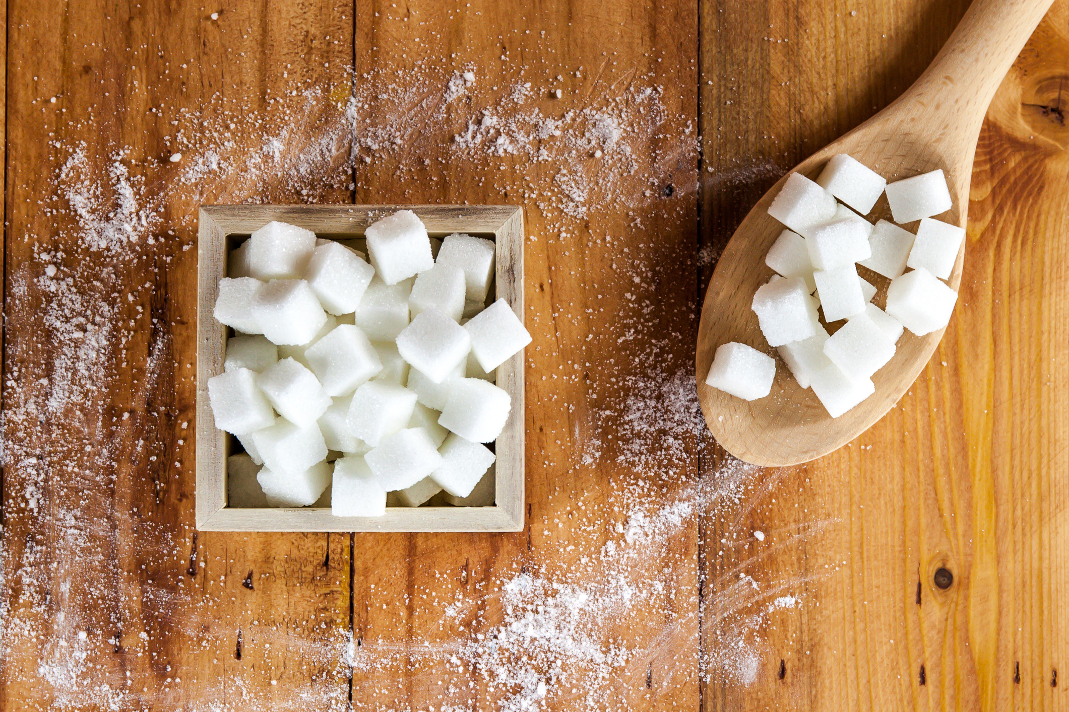 Sugar cubes in a box next to a wooden spoon filled with sugar cubes.