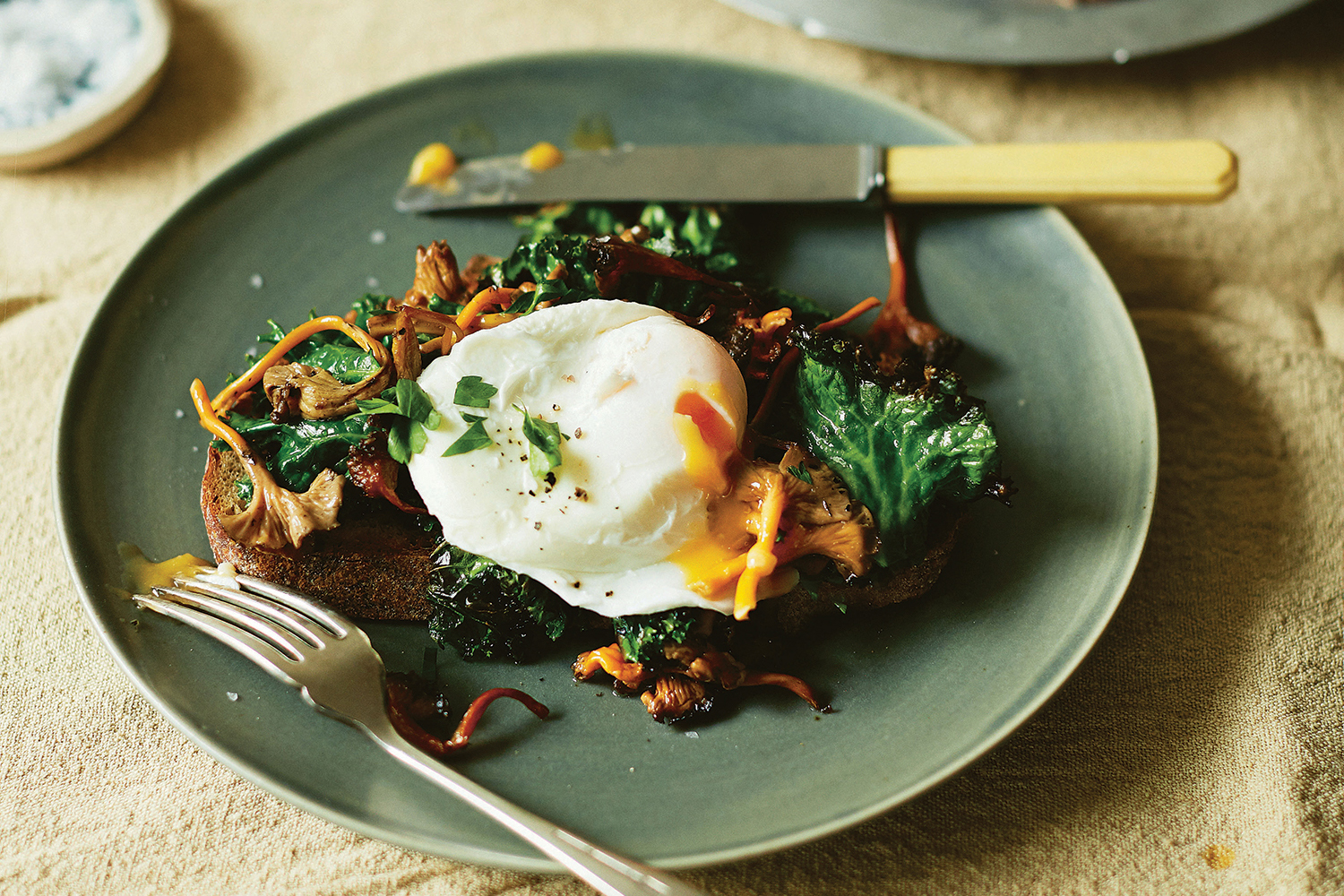 Chanterelle Toast with Poached Eggs and Kale on a plate with yolk pouring out of the egg.