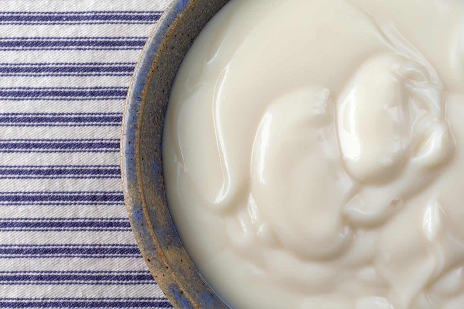 A top view of a bowl of vanilla yogurt with a blue and white striped background.