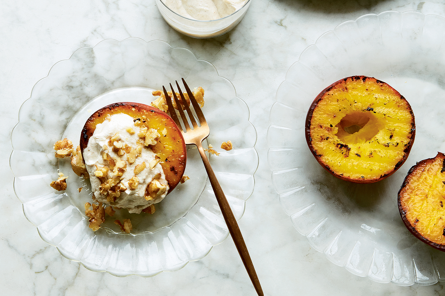 Grilled Peaches with Ginger Cream and Walnut Praline on a glass plate with brass fork.