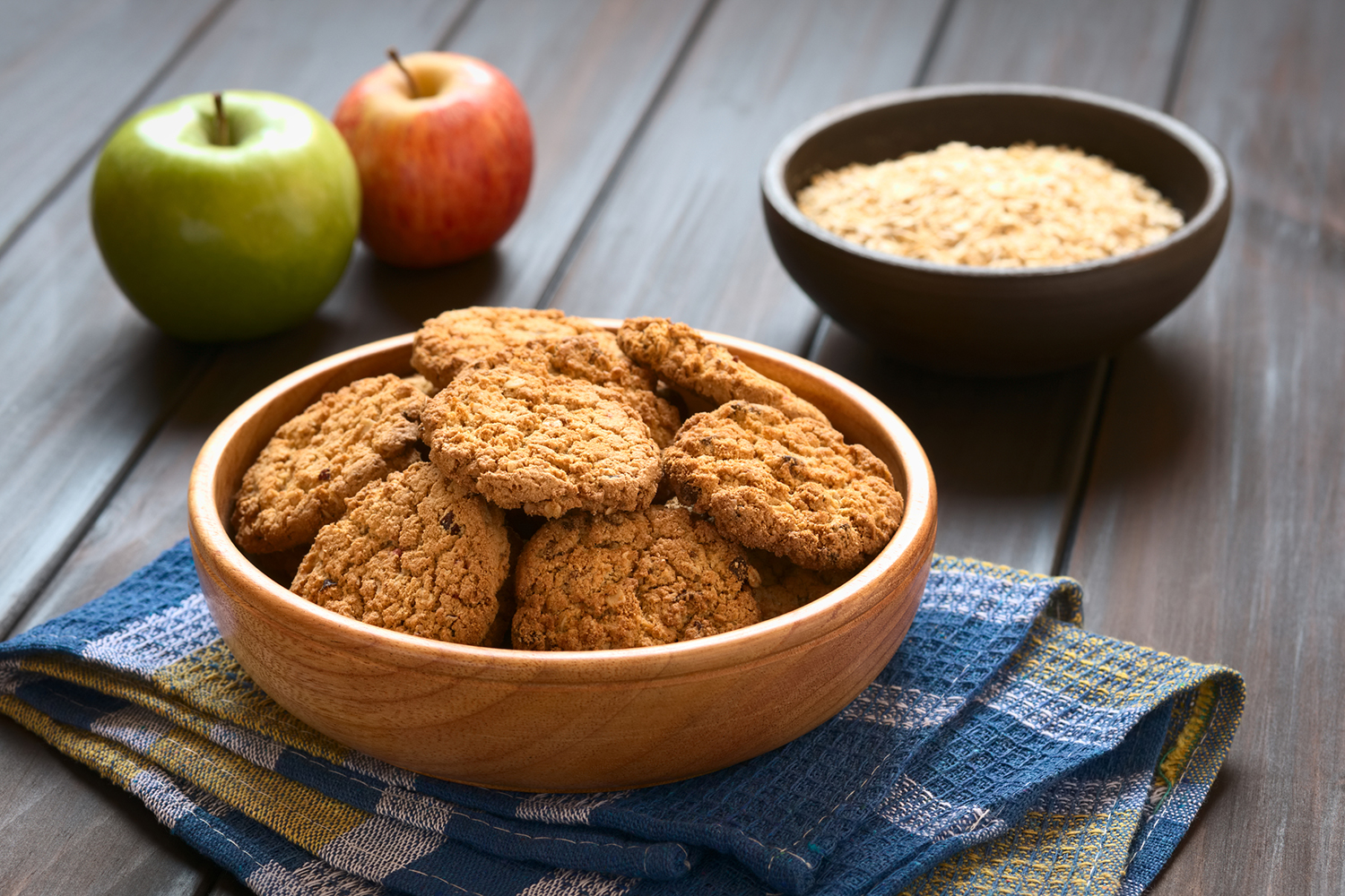 Apple Pie Cookies in wooden bowl with apples and oatmeal in the background.