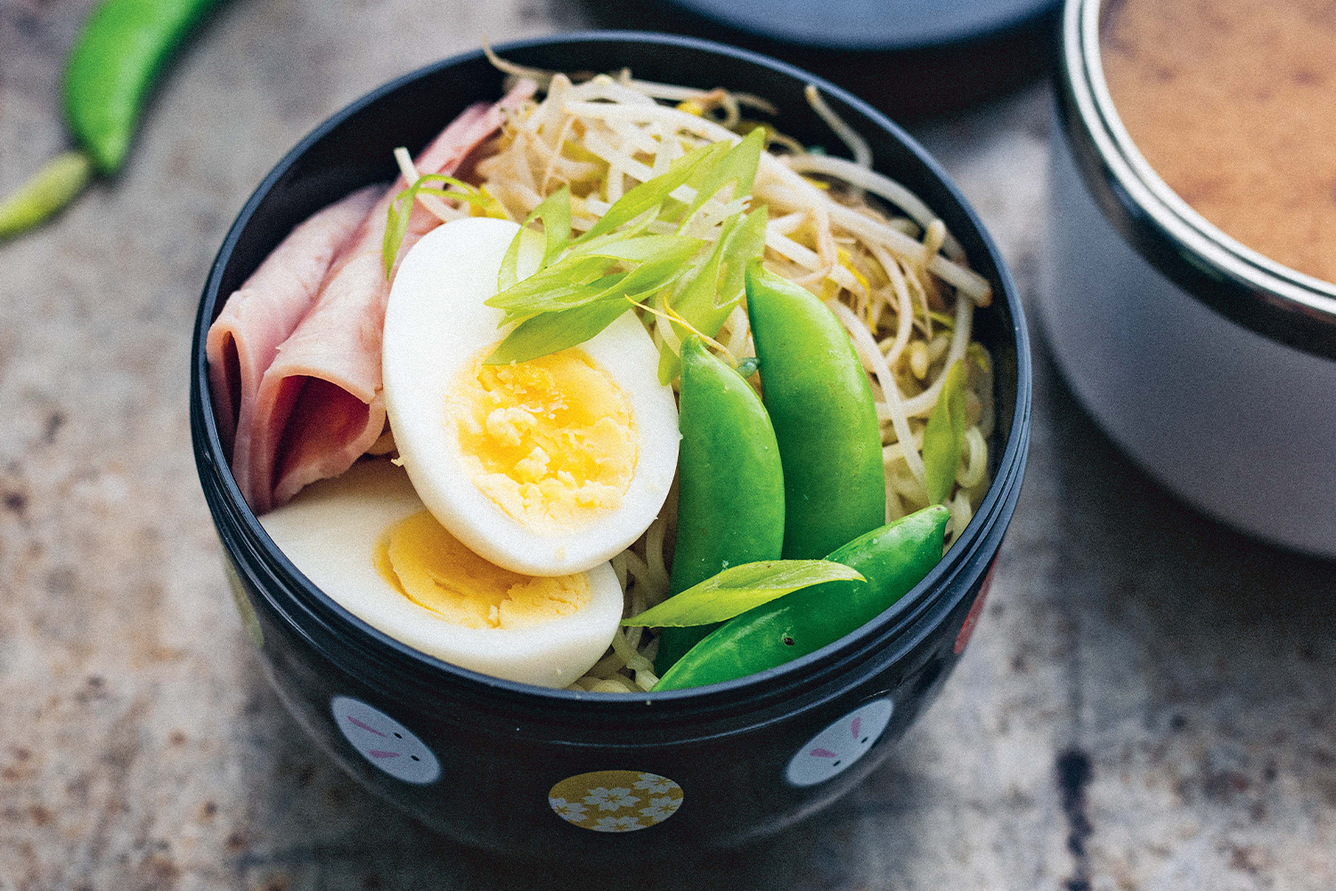 a bowl of noodles topped with ham, egg, and snow peas
