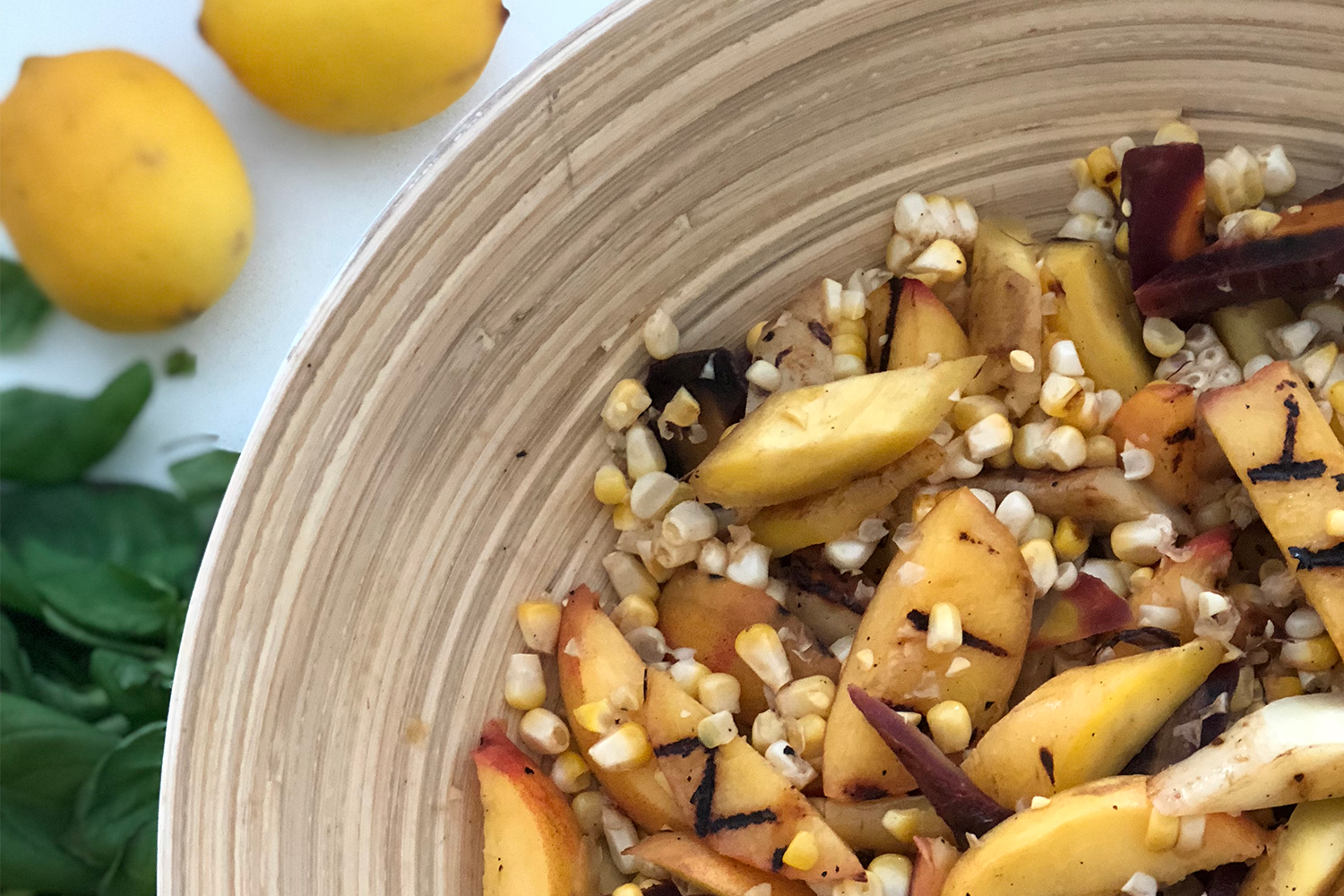 A bowl of salad with corn, peaches, carrots, and arugula