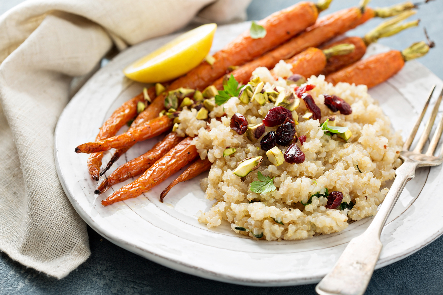 Quinoa salad with pistachios served on a white plate with roasted potatoes.