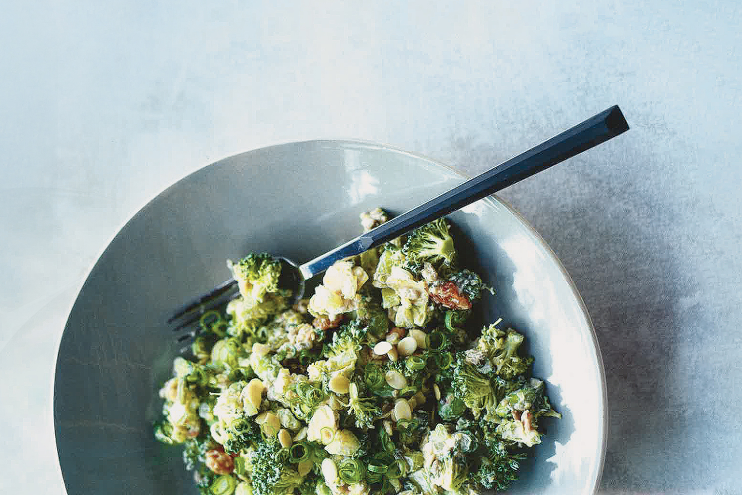 Raw Broccoli Salad in a light blue ceramic bowl on a light gray blue background.
