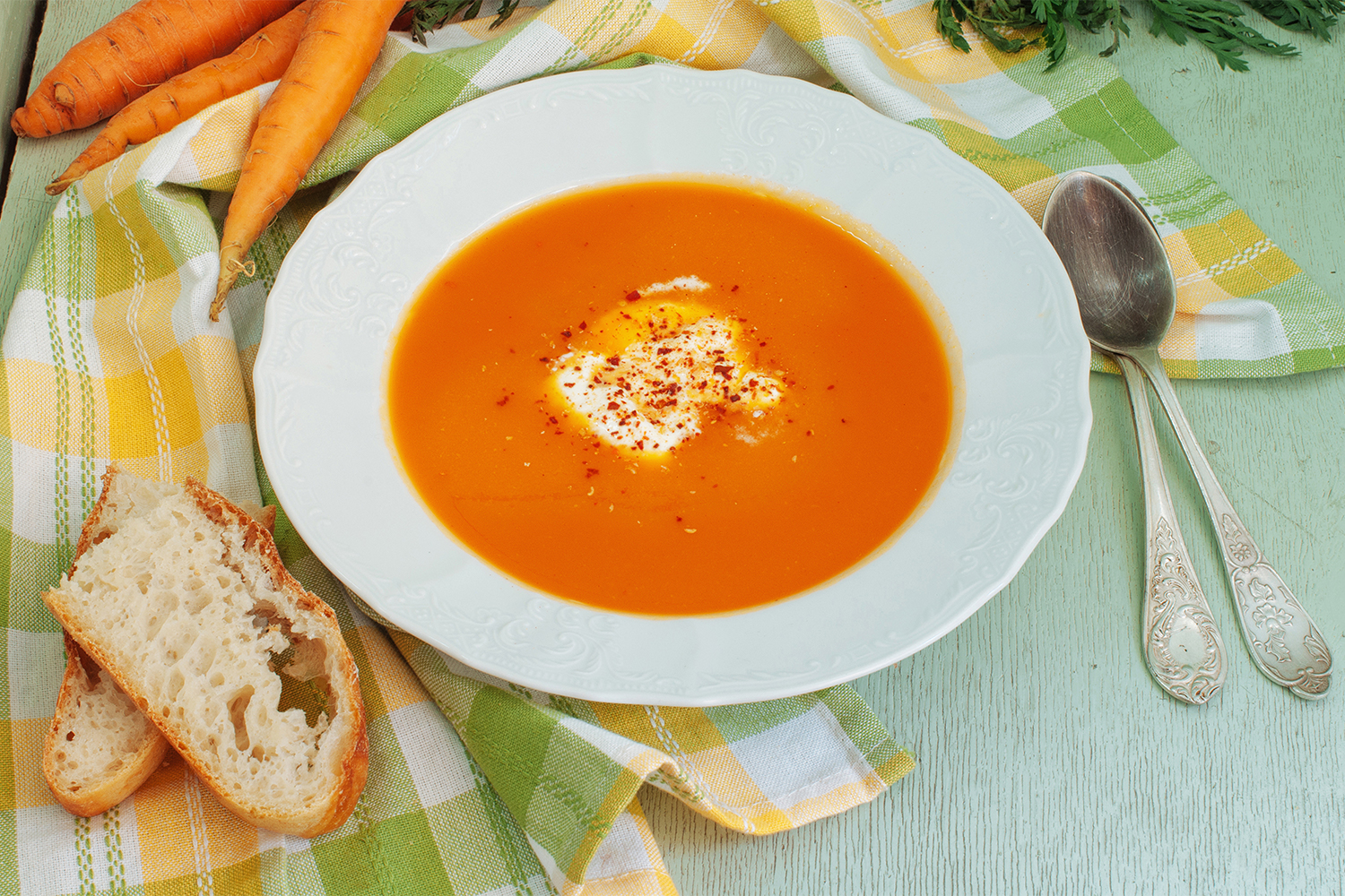 A bowl of carrot and apple soup with bread on the side