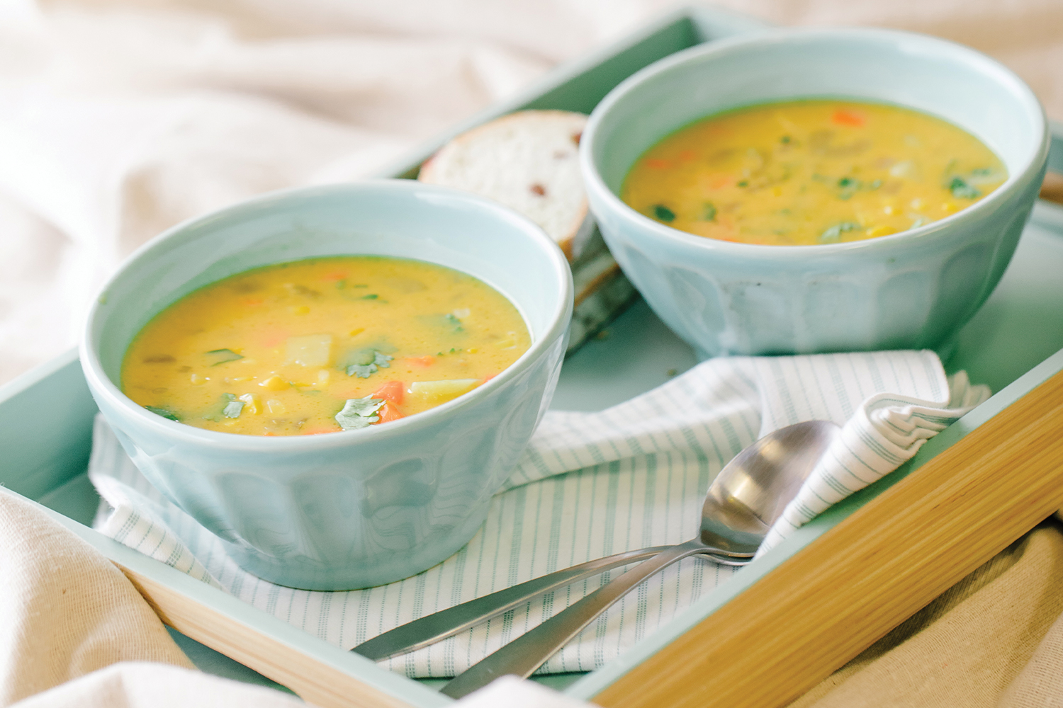 Two light blue bowls of coconut corn chowder on a bamboo serving tray.