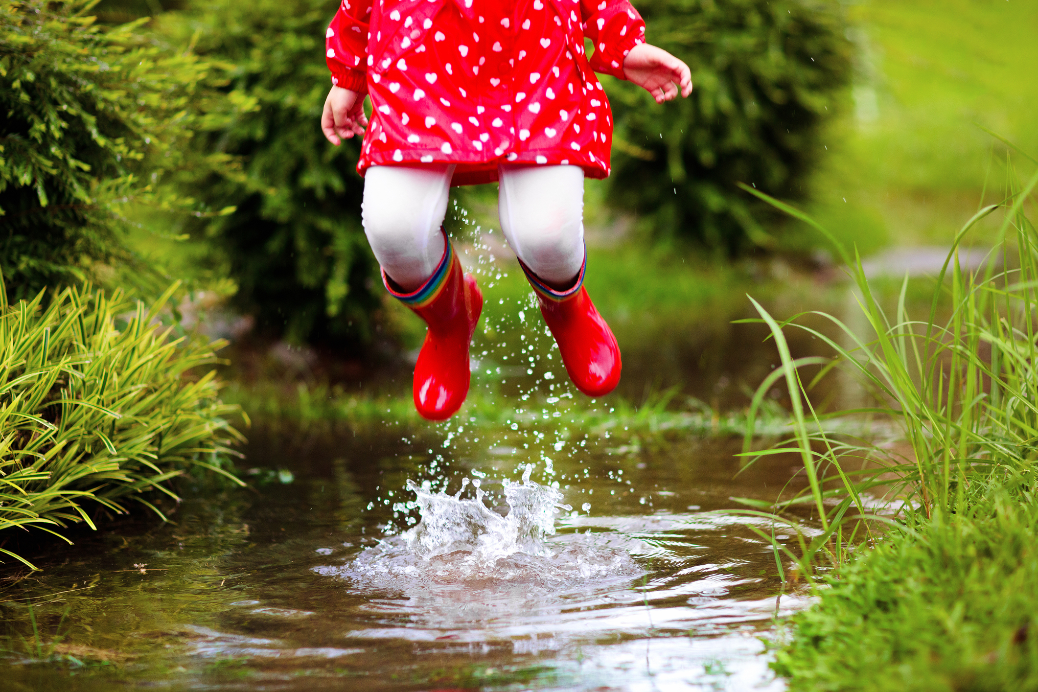 Young girl with red rubber boots jumping up from a creek.