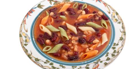 Colorful bowl of minestrone soup in a white bowl with floral decorative elements on rim.