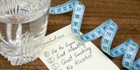 A list of New Year's resolutions next to a glass of water and measuring tape.
