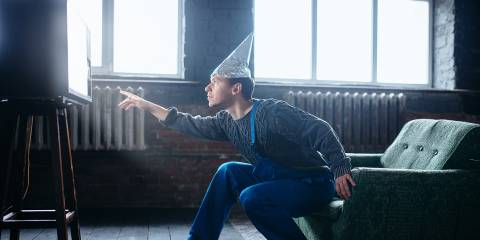 a man in a tinfoil hat reaching to the glow of a television