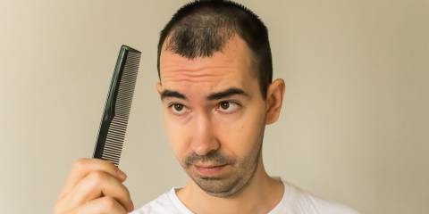 a middle-aged man looking at his comb with worry