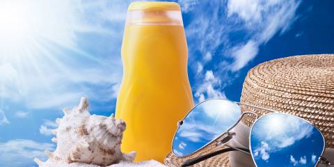 a bottle of sunscreen, a seashell, and a hat with a pair of sunglasses in the sand