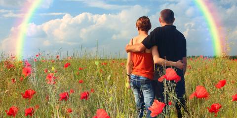 a couple in a field looking toward a rainbow