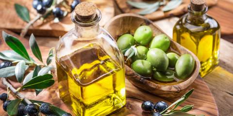 Olive oil, Berries on a branch and olives in a bowl placed on a wooden cutting board.