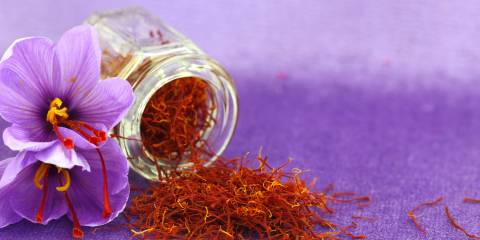 A small jar of saffron next to a saffron flower