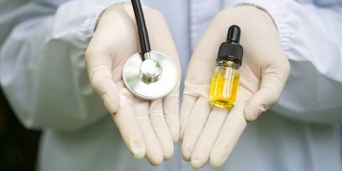 A Dr.'s hands holding a stethoscope and a bottle of CBD oil.