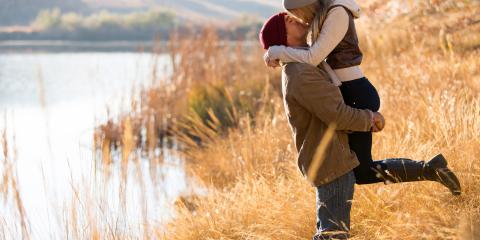 Man holding a woman in the air beside a mountain lake in autumn.