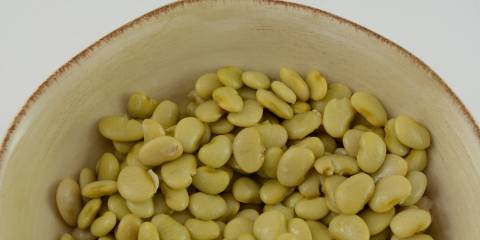 Top view of lima beans in cream colored rustic bowl with a white background.