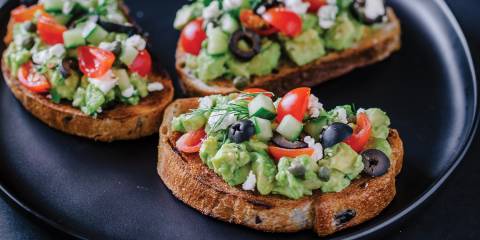 Greek Avocado Toast on a black plate with a black background.