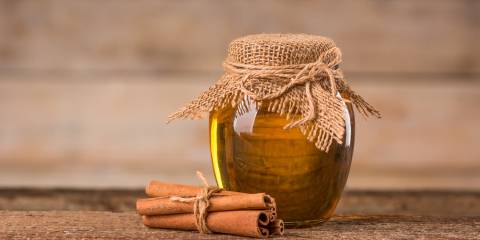 A jar of honey and cinnamon on a wooden background.