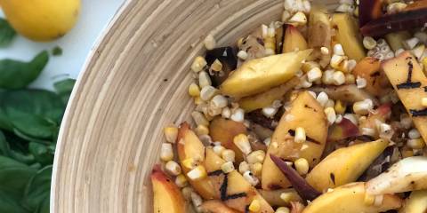 A bowl of salad with corn, peaches, carrots, and arugula