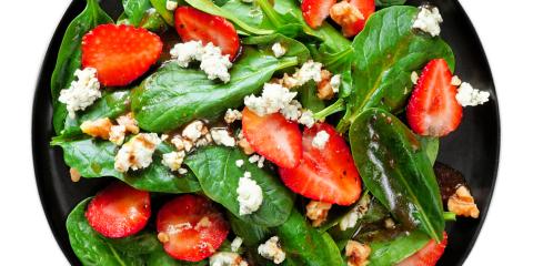 Black salad bowl filled with baby spinach, sliced strawberries, and blue cheese.