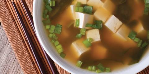 Miso Soup with Mushrooms, Bok Choy & Tofu in a white bowl placed on a white mat next to chop sticks.