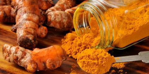 A jar of ground turmeric next to fresh roots.