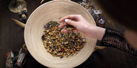 a woman mixing medicinal herbs near a smudge stick and a candle