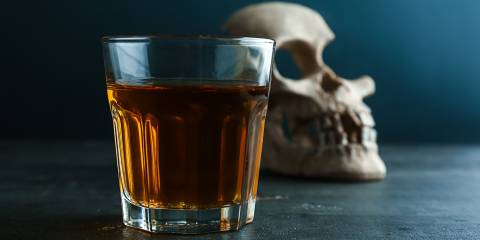 Glass of whiskey with skull on table