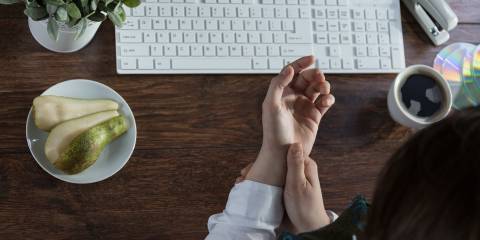 A woman massaging her inflamed wrist in front of a keyboard